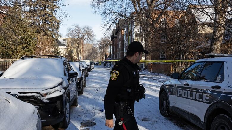 A police officer walks on a street next to parked cars.