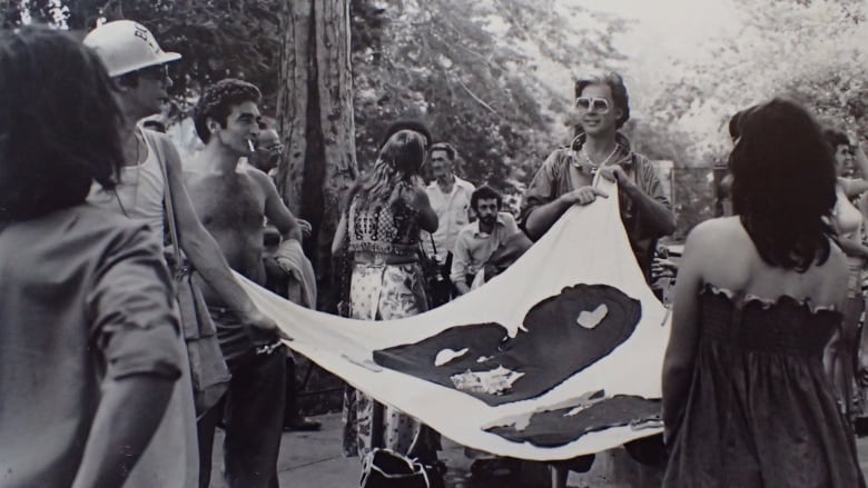 A black and white photo of people holding a large flag at a march. 