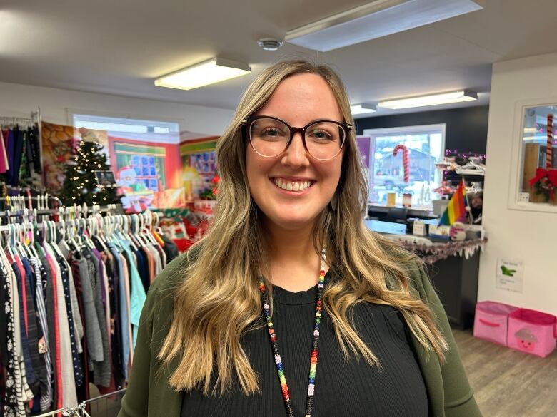 A Woman with glasses stands in front of clothing racks.