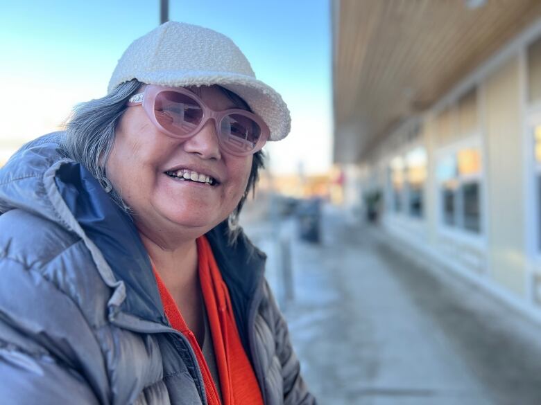 A woman with pink glasses, white ball cap and dark coat. 