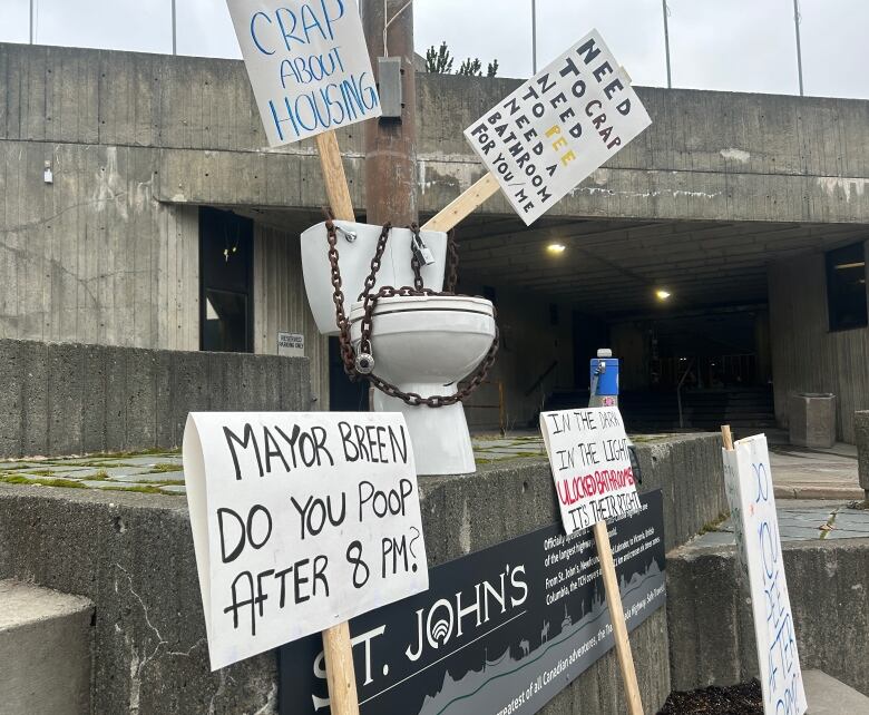 A toilet surrounded by signs placed on a concrete step in front of a government building. 