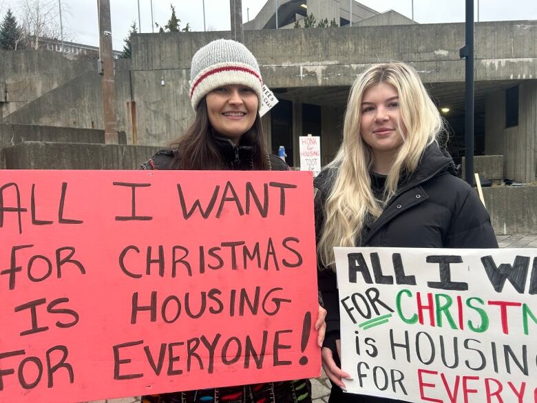 Two women holding protest signs in front of a government building. 