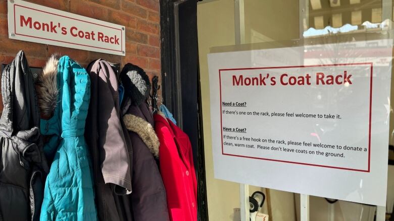 A coat rack is pictured outside a dry cleaner. A sign on the right explains that people are welcome to donate or take coats.