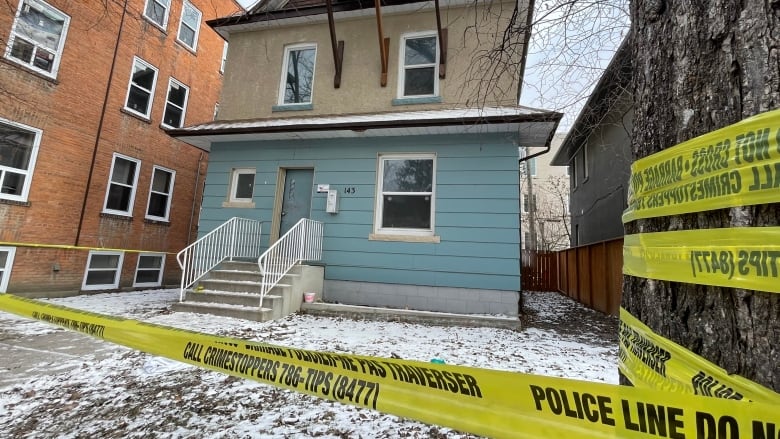 A home with blue and tan paneling is surrounded by police tape. 