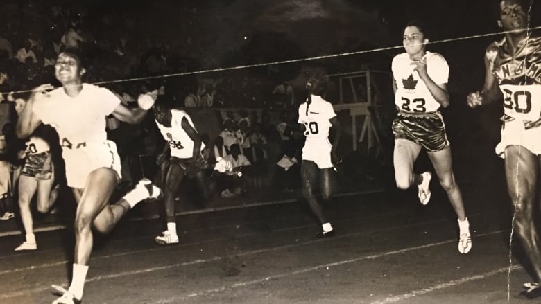 A woman lunges to the finish line in a race as other athletes train in the background. 