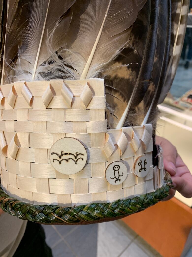 A woven wooden headdress adorned with feathers and three small symbols.