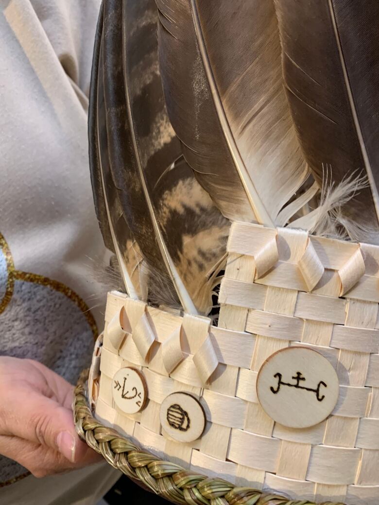 A woven wooden headdress adorned with feathers and three small symbols.