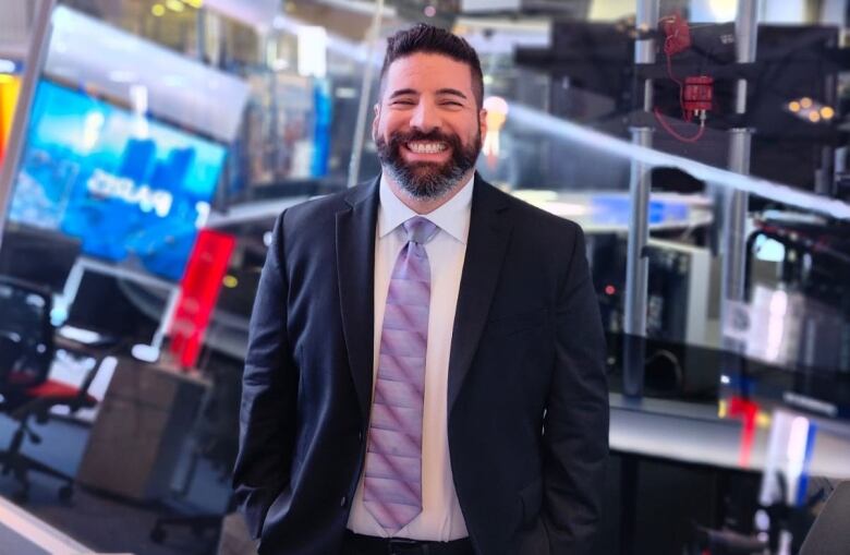 A man in a suit smiles for a photo in a studio.