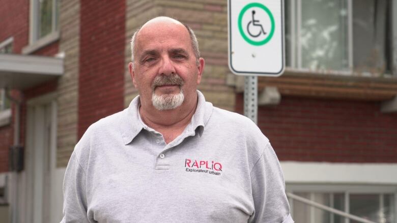 Man wearing a polo with the logo RAPLIQ stands beside handicapped parking sign.