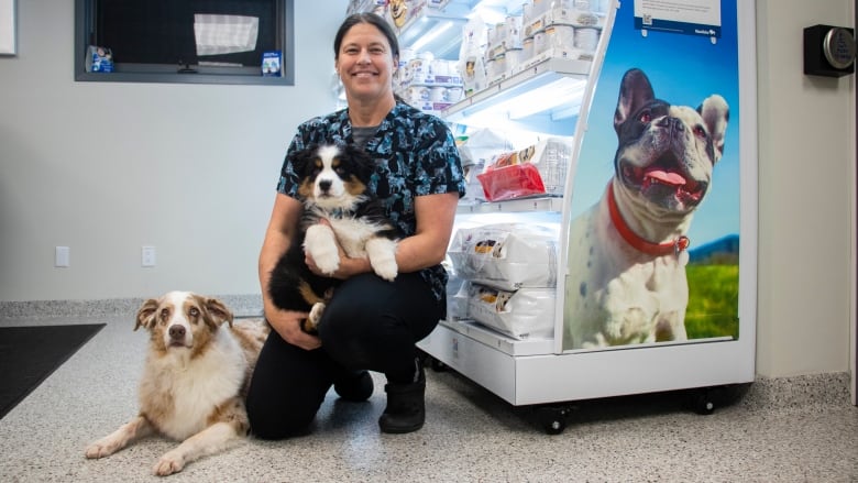 A woman kneels with a puppy and a dog.