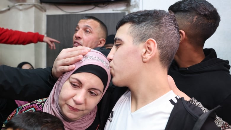 A teenage boy wraps his hand around the head of a woman in a pink headscarf and kisses her. 