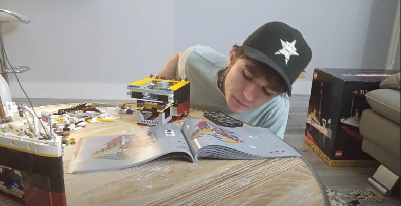 Man in baseball hat sitting behind table building a Lego Titanic.