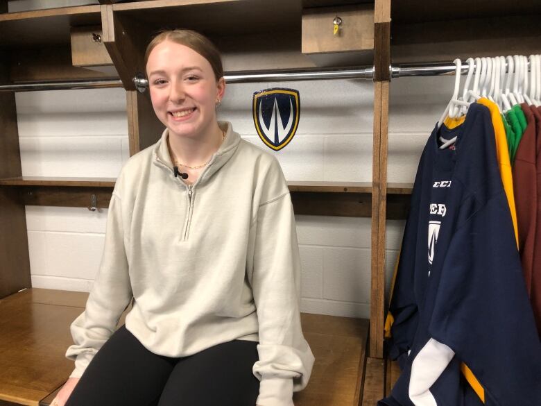 A girl wearing a beige sweater sitting in a hockey changing room