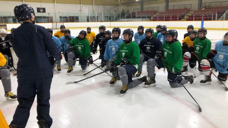 A bunch of women's hockey players on one knee while their coach instructs them on their next drill