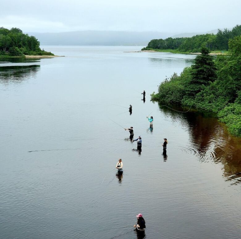 From a far distance, eight anglers can be seen in a large, calm river. 