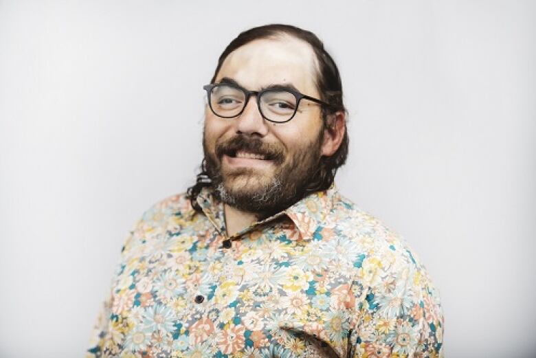 A man with glasses, a brown beard and hair, wearing a floral print shirt.