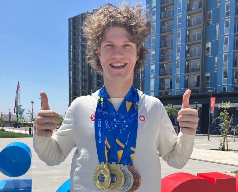 A smiling man with four medals around his neck giving two thumbs up