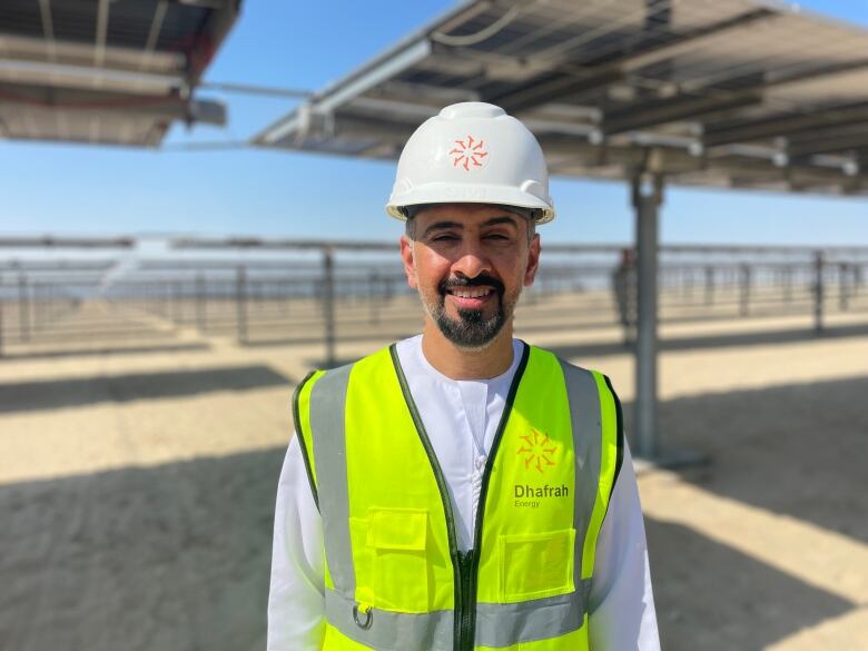 Man in yellow safety vest and white helmet stands amid field of solar panels