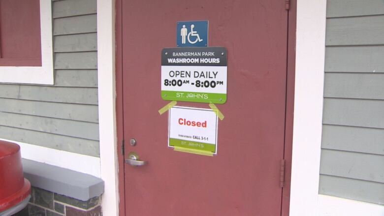 A red washroom door with two signs on it. One sign reads the washroom is open from 8 a.m. to 8 p.m., but the other reads 'Closed' in red lettering.