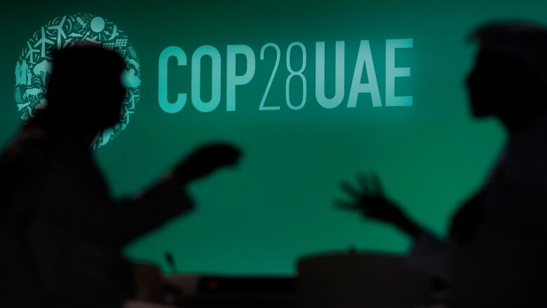 People are silhouetted against a green backdrop with the words COP 28 U-A-E.