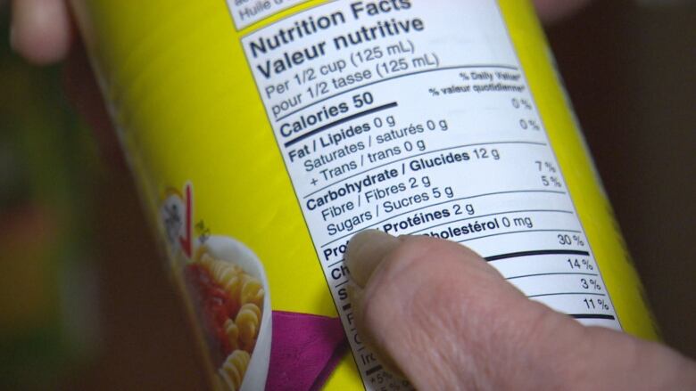 A close up of a can of spaghetti sauce, with a finger pointing to the line of the nutritional facts label stating the sauce contains 5 grams of sugar per half cup.