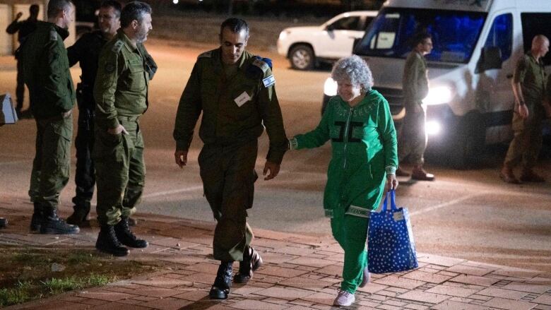 An elderly woman walks with an Israeli soldier.