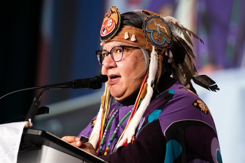 Woman in headdress speaks at a microphone and podium.