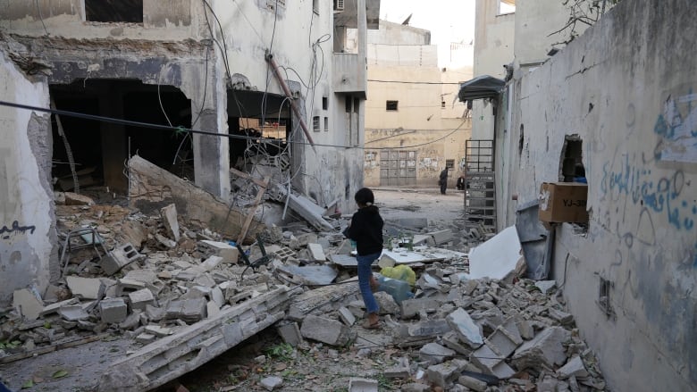 A girl walks over blocks of concrete and other debris from destroyed buildings littering a street.