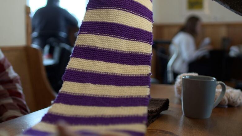 A purple and white scarf is held over a coffee table. A mug is nearby. 