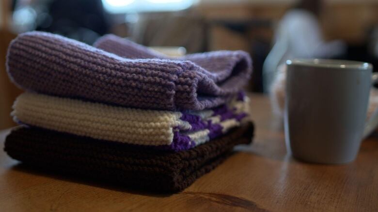 A stack of folded woolen scarves sits on a table. 