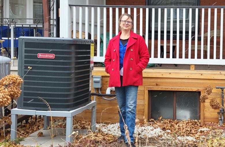 Woman stands beside a heat pump fan.