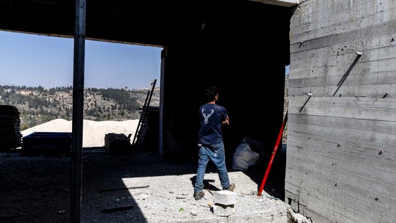 A construction worker in jeans and a navy blue T-shirt walks through a concrete building.