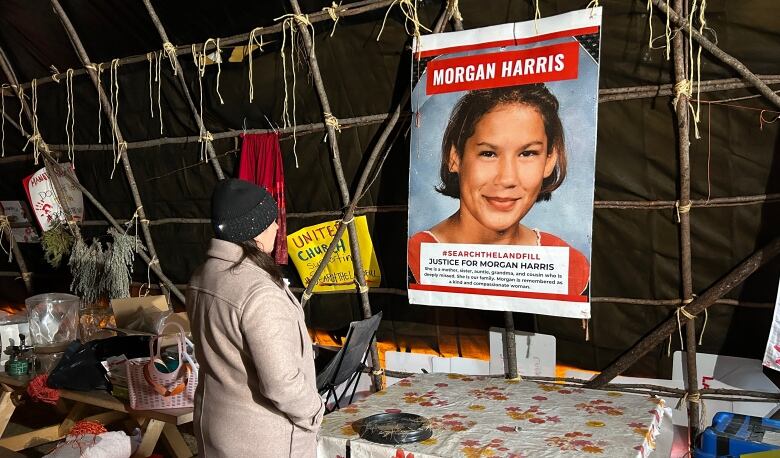 A woman wearing a toque and a cream-coloured coat looks at an image of another woman with the name Morgan Harris on it.