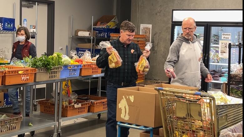 Three volunteers are loading food into cardboard box food hampers at the Central Okanagan Food Bank in Kelowna, B.C. 