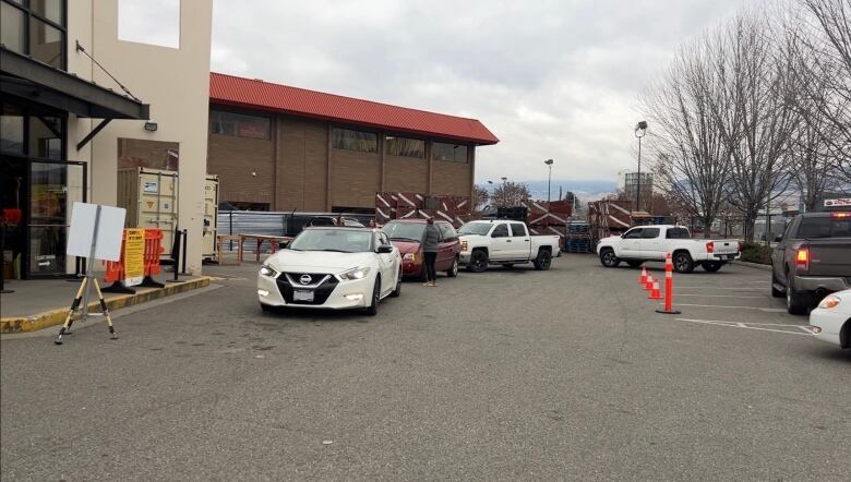 A line up of 6 vehicles outside the food bank's Kelowna warehouse as clients wait for volunteers to bring their food hampers on a cloudy morning. 