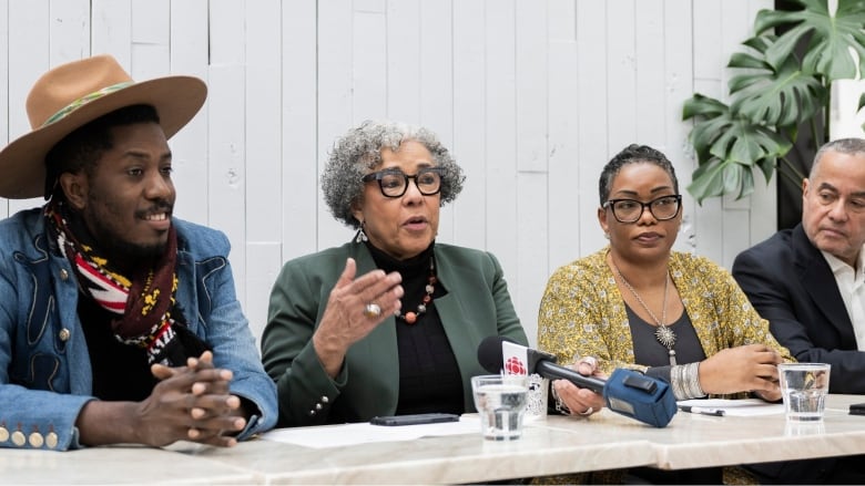 four people sit behind a table during a news conference. 