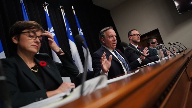 Christine Frchette rubs her head while Franois Legault speaks to the media during a press conference. 