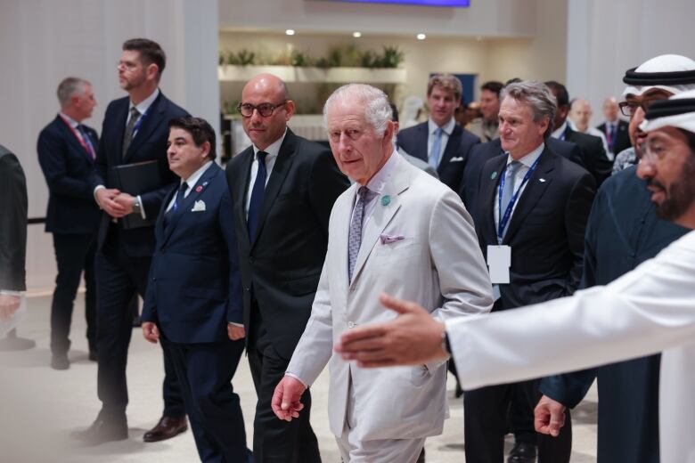 King Charles is pictured walking with a group of people in the hallway of a conference venue.