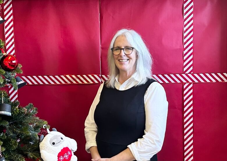 A smiling woman with shoulder-length, white hair stands in front of a door wrapped in red.