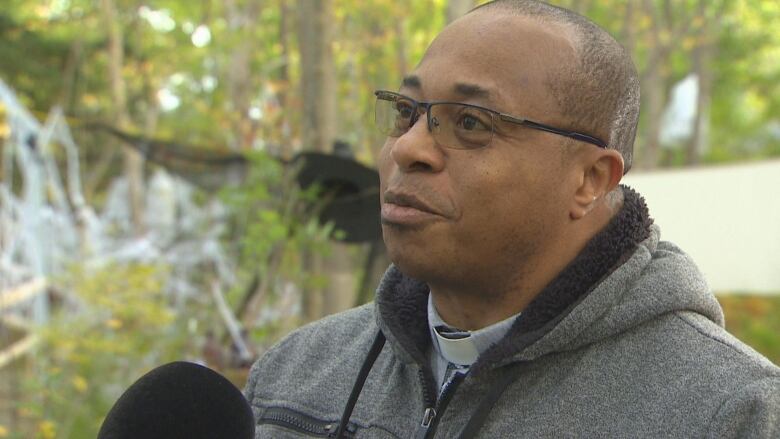 A man wearing glasses stands outside in front of a microphone.