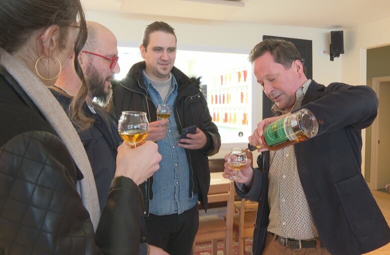 A man surrounded by people pours whisky into a glass.