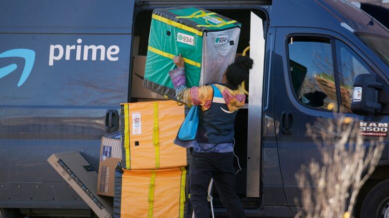 A worker in black-and-blue vest lifts a large package out of an Amazon delivery truck.