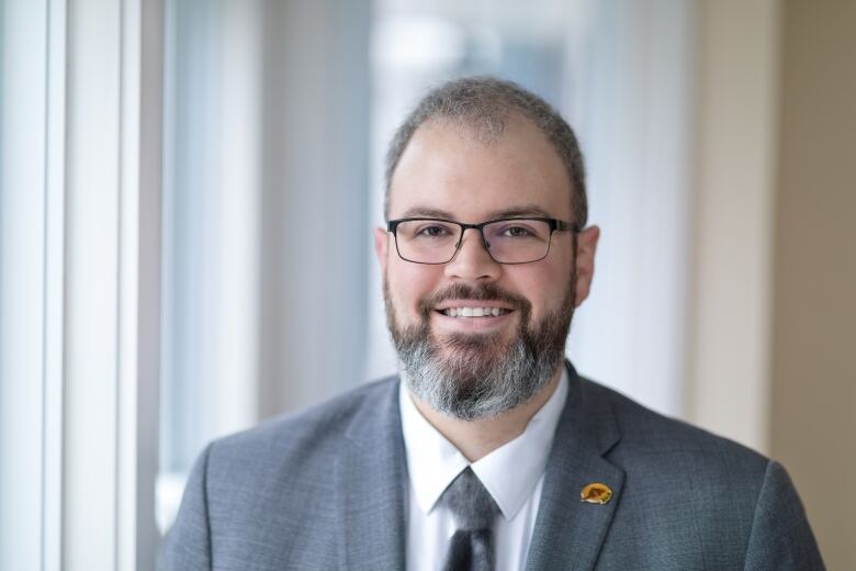 A spectacled man in a grey suit.