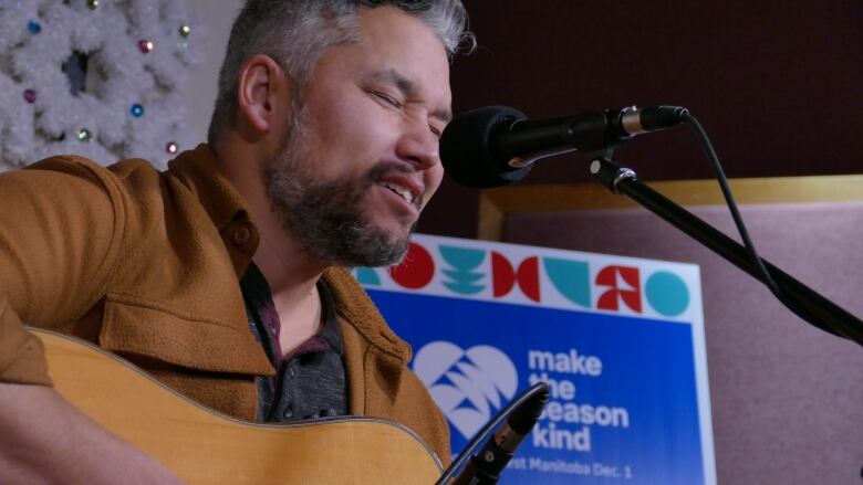 A man sings into a microphone as he plays an acoustic guitar.