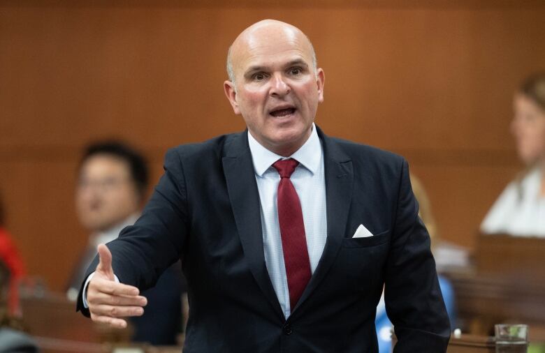 A man in a black suit and red tie gestures with his hand as he speaks in the House of Commons.