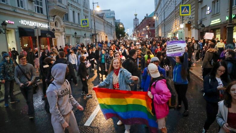 A woman is surrounded by fellow demonstrators as she holds a rainbow LGBTQ pride flag.