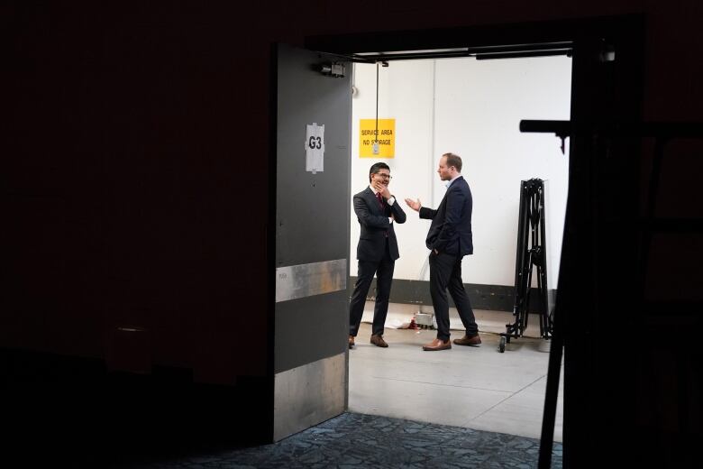 Two men are seen through a doorway talking.