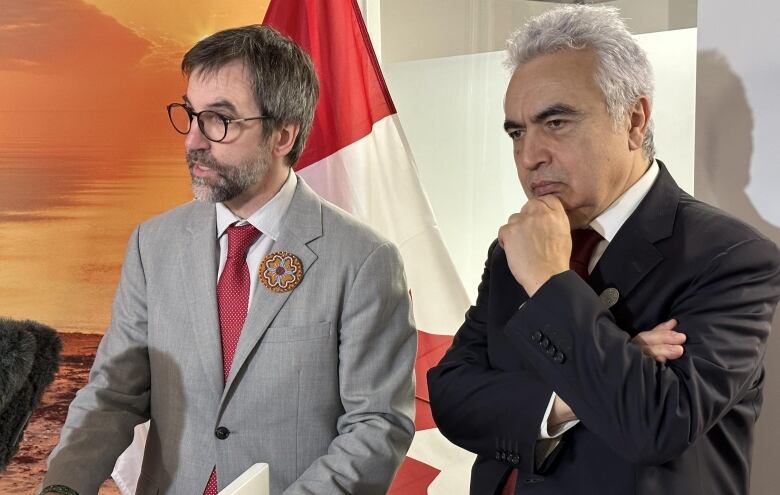 Two men speak at a podium with a Canada flag in the background.