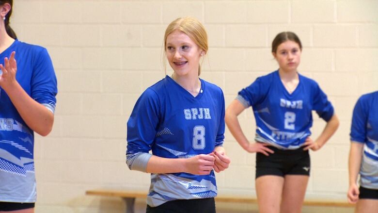 A young girl wearing a blue jersey stands in a school gym.