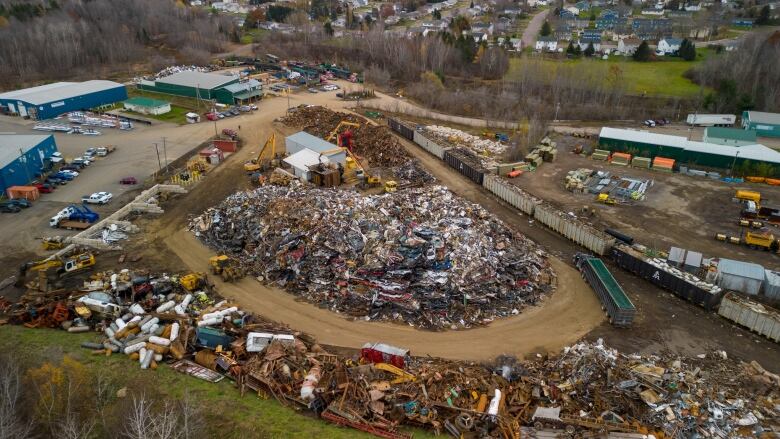 A large pile of scrap material with residential properties in the background.